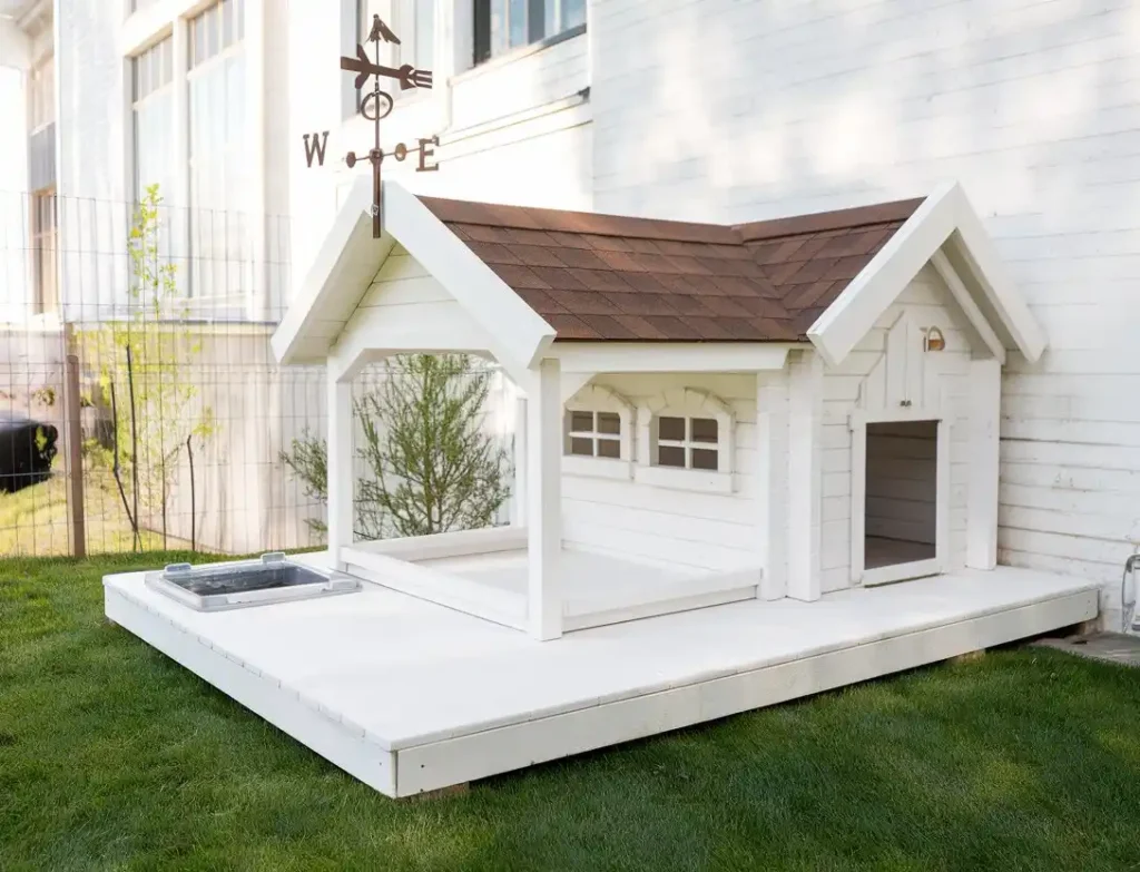 White dog house with brown roof, weather vane, and attached covered run area